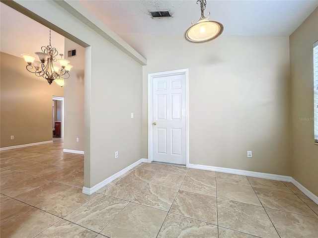 tiled spare room featuring a notable chandelier and a textured ceiling