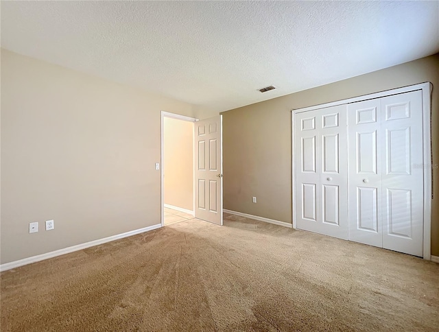 unfurnished bedroom featuring a closet, a textured ceiling, and light colored carpet