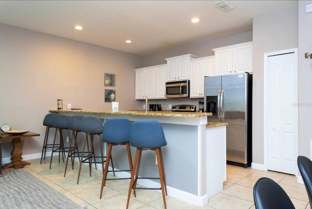 kitchen featuring a kitchen breakfast bar, light stone counters, white cabinets, light tile patterned floors, and stainless steel appliances