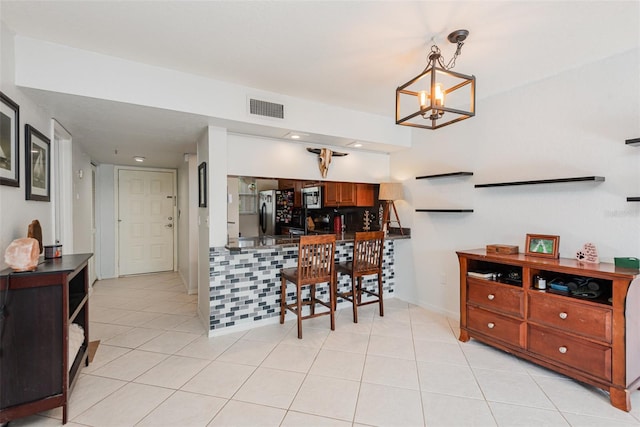 kitchen featuring light tile patterned floors, kitchen peninsula, appliances with stainless steel finishes, a notable chandelier, and decorative light fixtures