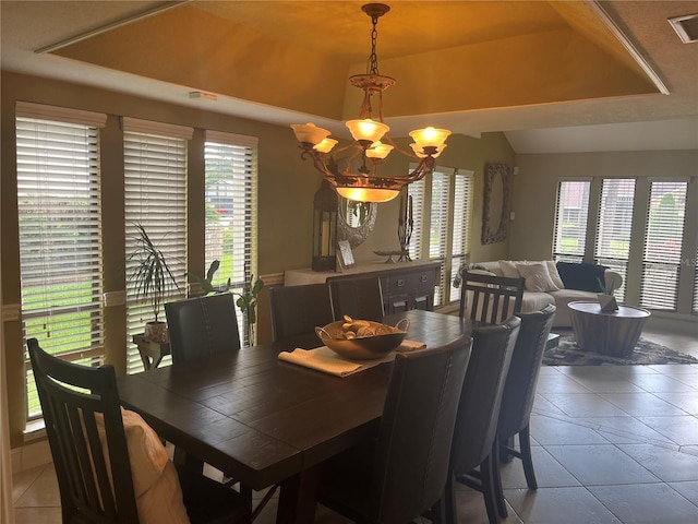 tiled dining room featuring a tray ceiling, plenty of natural light, and a chandelier