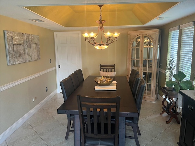 tiled dining space with a tray ceiling and a chandelier