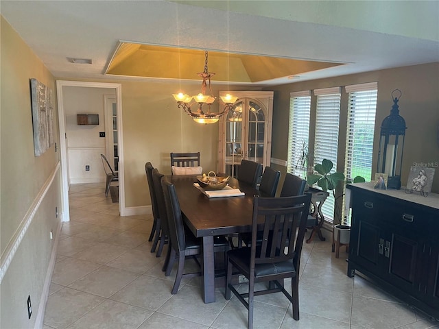 tiled dining area with a tray ceiling and a chandelier