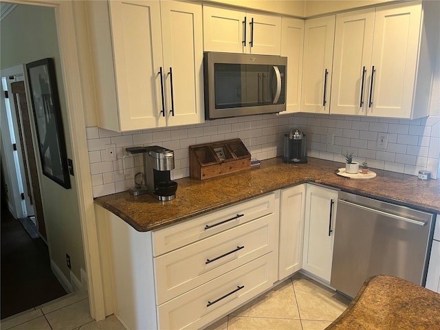 kitchen with white cabinetry, light tile patterned floors, dark stone counters, and appliances with stainless steel finishes