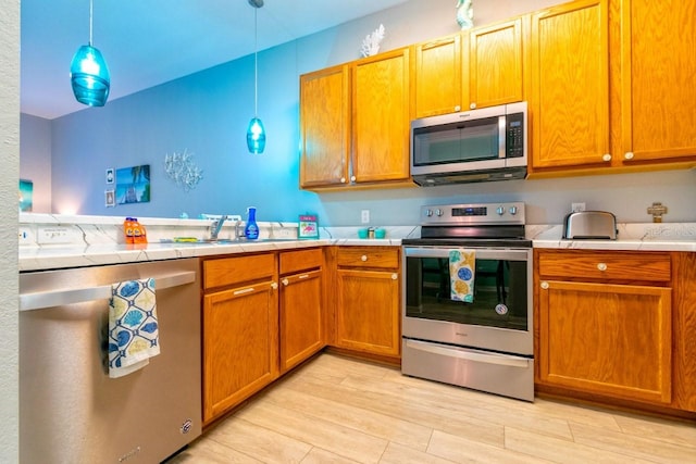 kitchen with pendant lighting, appliances with stainless steel finishes, sink, and light hardwood / wood-style floors