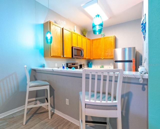 kitchen featuring stainless steel appliances, hanging light fixtures, light hardwood / wood-style flooring, kitchen peninsula, and a kitchen breakfast bar