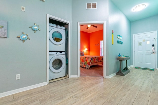 laundry room featuring stacked washer and clothes dryer, light hardwood / wood-style floors, and ceiling fan