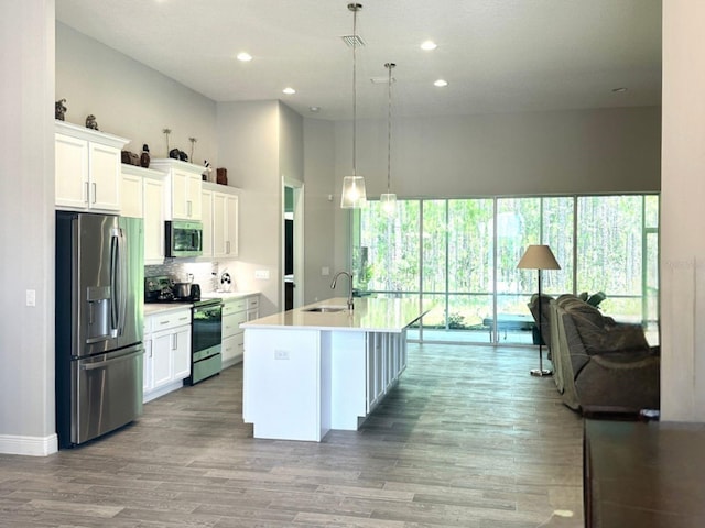 kitchen with a center island with sink, sink, white cabinetry, hanging light fixtures, and appliances with stainless steel finishes