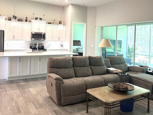 living room with light wood-type flooring, a high ceiling, and sink