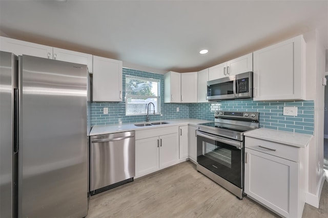 kitchen with sink, tasteful backsplash, white cabinetry, light hardwood / wood-style floors, and stainless steel appliances