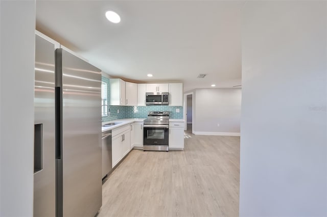 kitchen featuring light hardwood / wood-style flooring, sink, white cabinetry, decorative backsplash, and stainless steel appliances