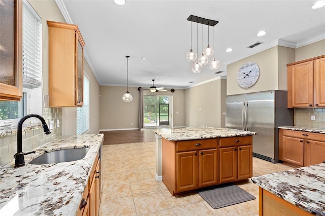 kitchen with ceiling fan, decorative light fixtures, a center island, sink, and stainless steel fridge