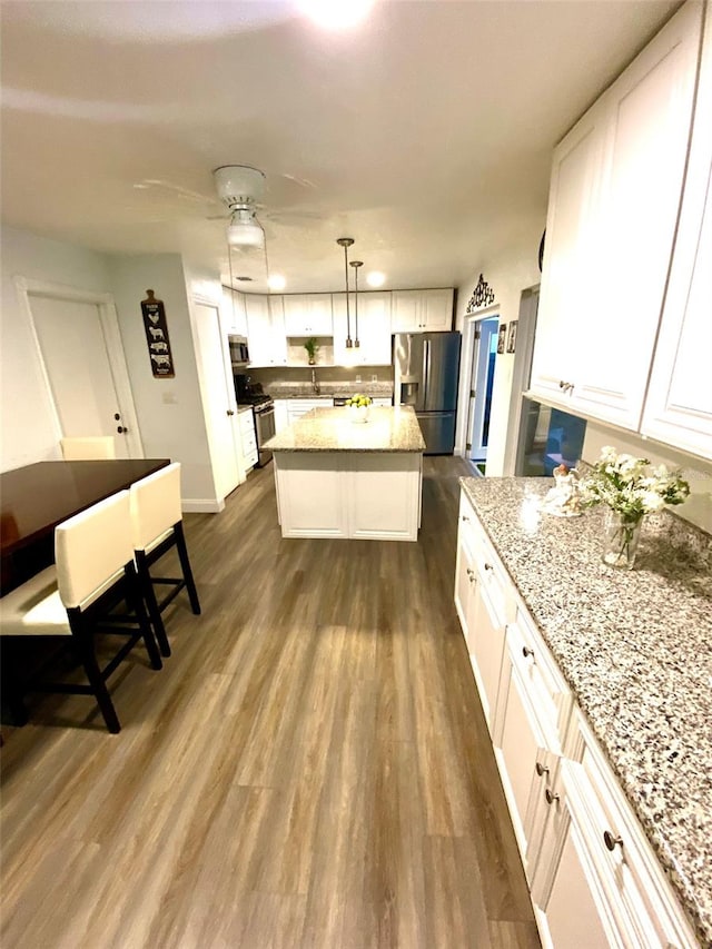 kitchen with dark hardwood / wood-style floors, stainless steel appliances, a center island, pendant lighting, and white cabinetry