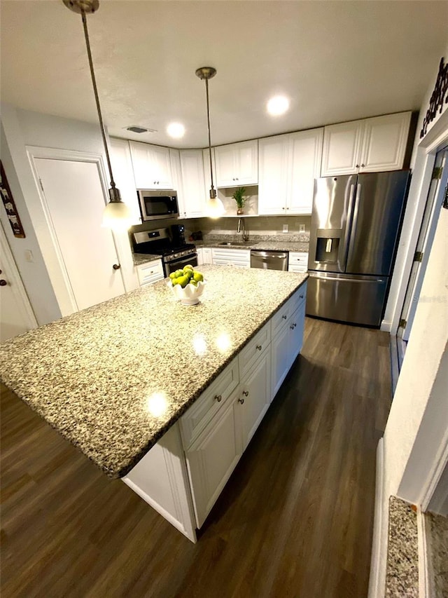 kitchen with white cabinetry, dark hardwood / wood-style floors, stainless steel appliances, decorative light fixtures, and light stone counters