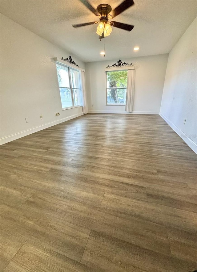 empty room with a wealth of natural light, dark wood-type flooring, a textured ceiling, and ceiling fan