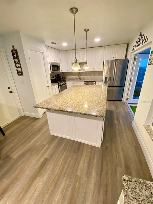 kitchen with hanging light fixtures, stainless steel appliances, hardwood / wood-style floors, light stone countertops, and white cabinetry