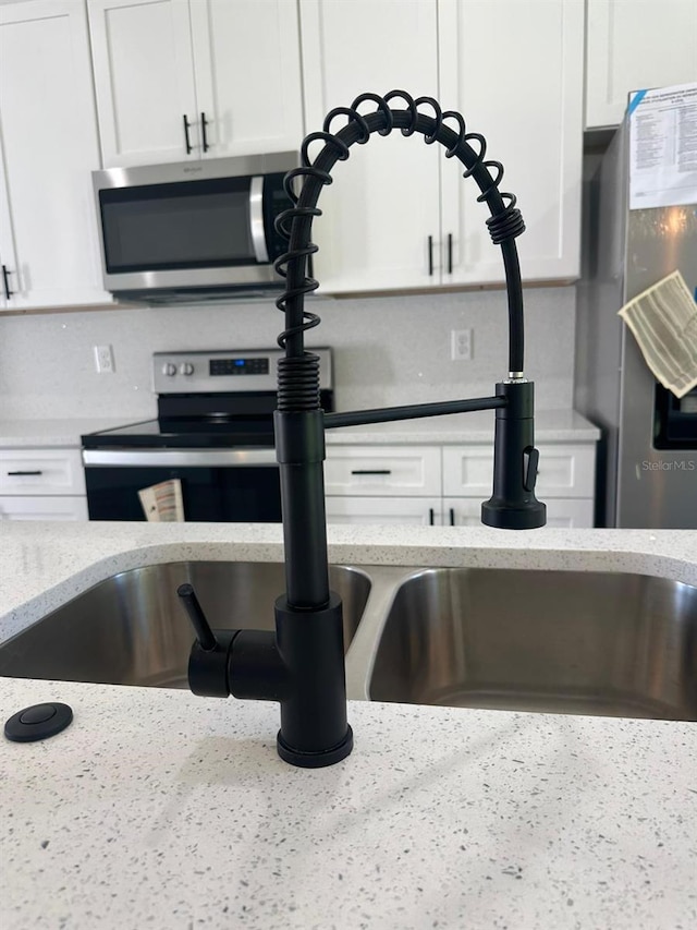 details featuring light stone counters, appliances with stainless steel finishes, sink, and white cabinets