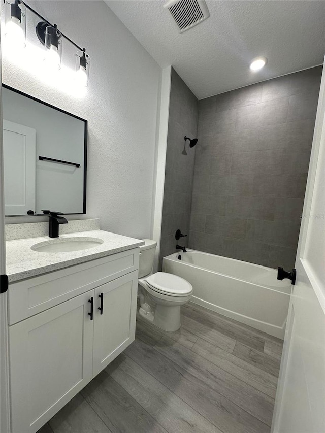 full bathroom featuring hardwood / wood-style flooring, toilet, tiled shower / bath combo, vanity, and a textured ceiling