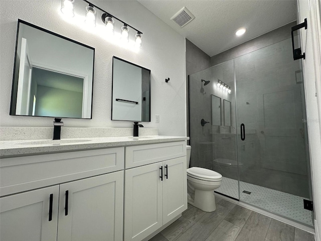 bathroom with hardwood / wood-style floors, vanity, a textured ceiling, a shower with shower door, and toilet