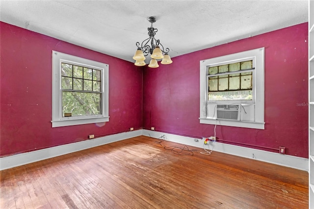 unfurnished room with hardwood / wood-style flooring, cooling unit, a textured ceiling, and a notable chandelier