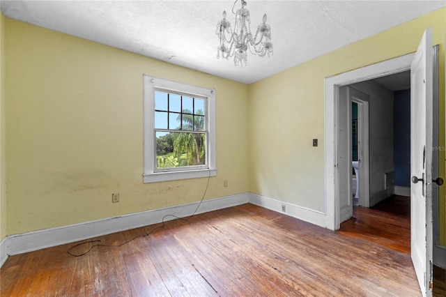 unfurnished room with hardwood / wood-style floors, a textured ceiling, and an inviting chandelier