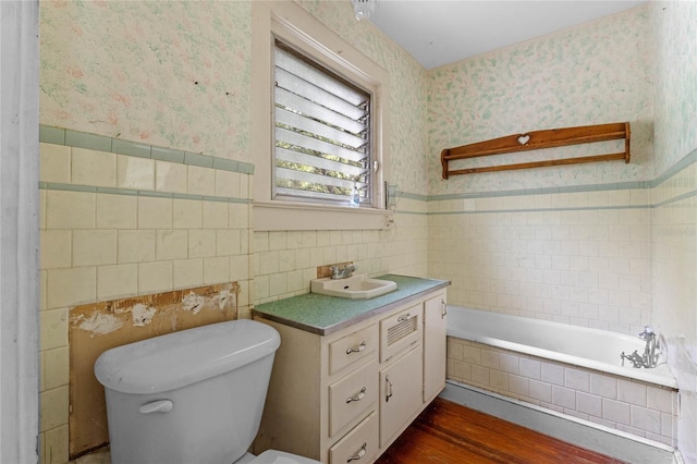 bathroom with tiled bath, tile walls, hardwood / wood-style flooring, vanity, and toilet