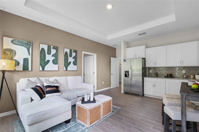 living room with sink, light hardwood / wood-style flooring, and a tray ceiling