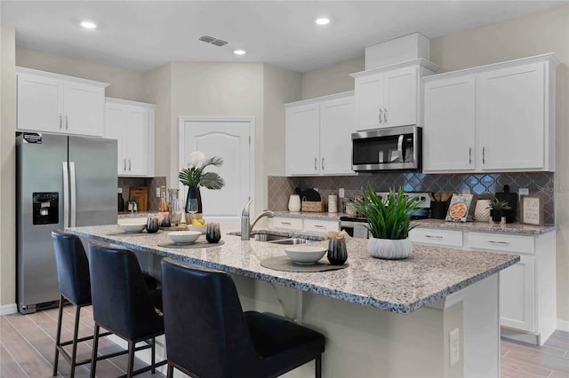 kitchen with appliances with stainless steel finishes, white cabinets, a center island with sink, and a sink