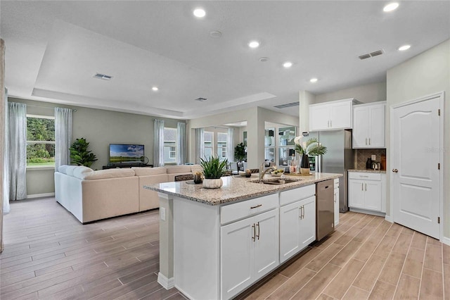 kitchen with a center island with sink, visible vents, white cabinets, appliances with stainless steel finishes, and open floor plan