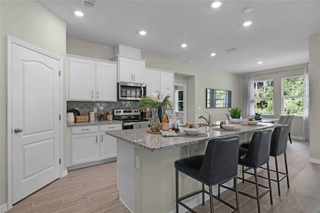 kitchen featuring a kitchen island with sink, wood finish floors, white cabinetry, appliances with stainless steel finishes, and light stone countertops