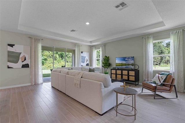 living area with visible vents, a tray ceiling, light wood-style flooring, and baseboards