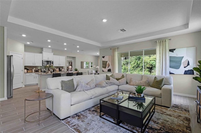 living area with a tray ceiling, wood finish floors, visible vents, and recessed lighting