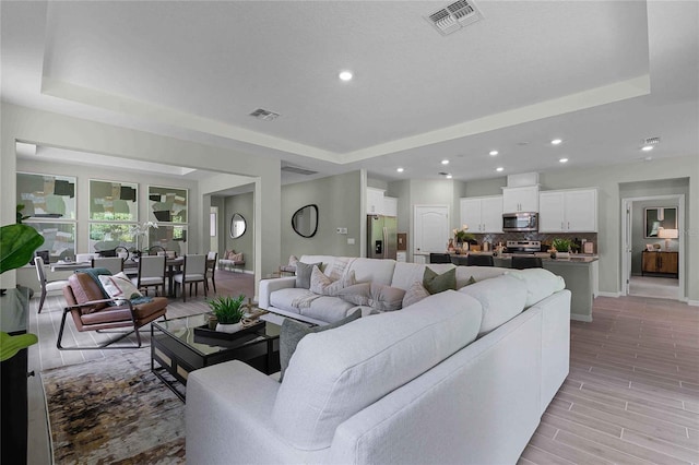 living area with a tray ceiling, visible vents, recessed lighting, and wood tiled floor