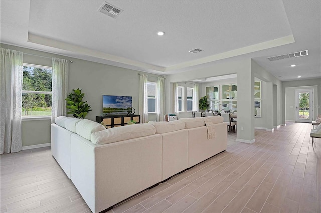 living area featuring light wood-style floors, visible vents, and a tray ceiling