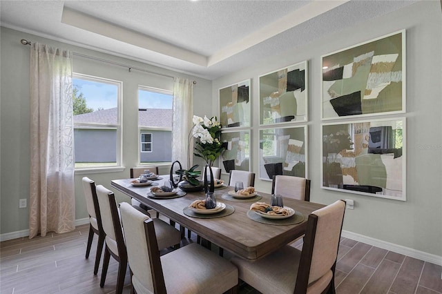 dining area with baseboards, a tray ceiling, a textured ceiling, and wood finish floors