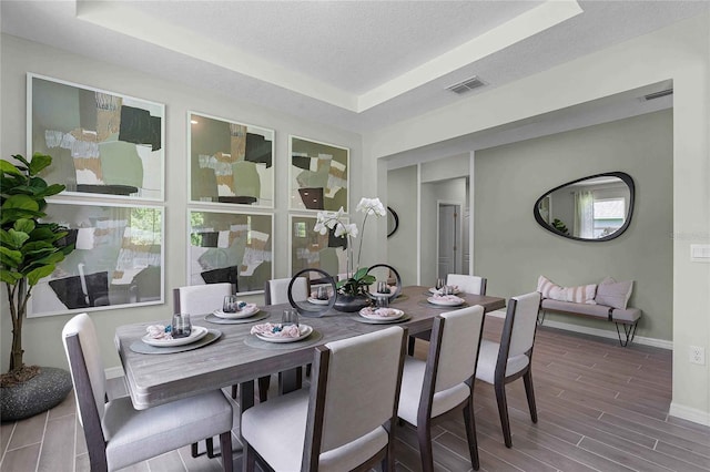 dining area featuring visible vents, baseboards, a raised ceiling, a textured ceiling, and wood finish floors