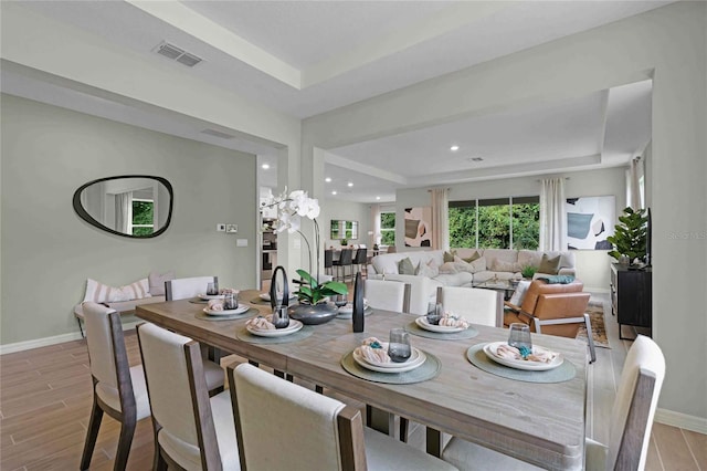 dining space featuring light wood-style floors, a raised ceiling, visible vents, and baseboards