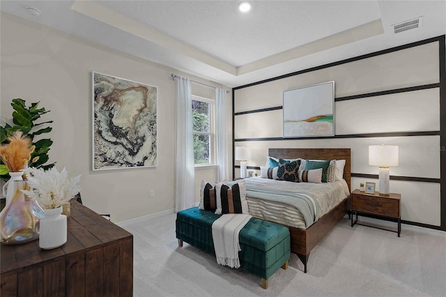 bedroom featuring a tray ceiling, light colored carpet, visible vents, and baseboards