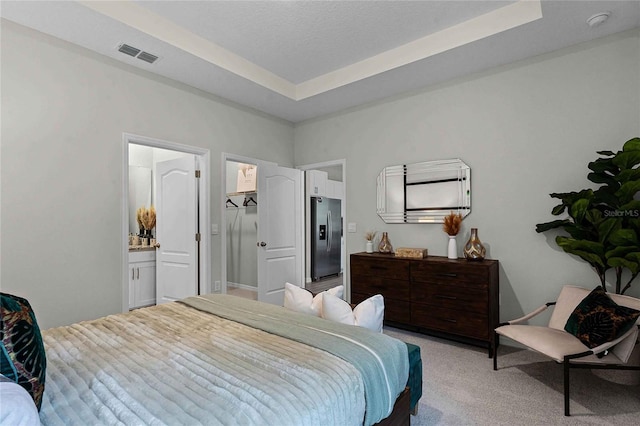 bedroom featuring a textured ceiling, light colored carpet, visible vents, stainless steel fridge, and a raised ceiling