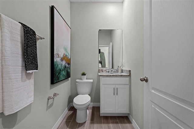 half bath featuring toilet, vanity, baseboards, and wood finish floors