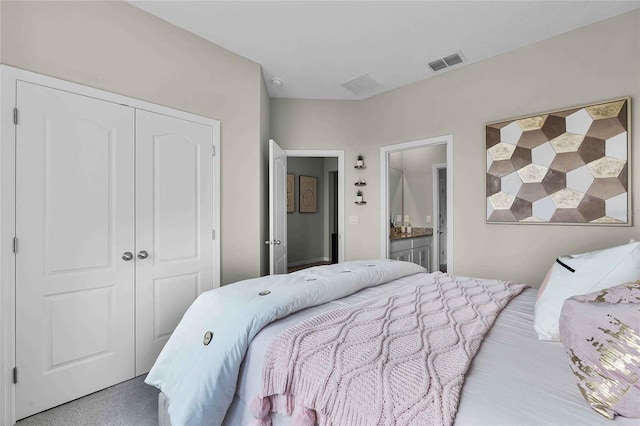 bedroom with a closet, connected bathroom, visible vents, and light colored carpet