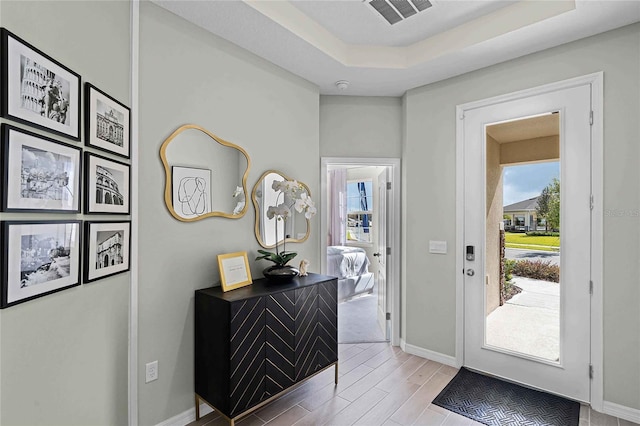 foyer with wood finished floors, a raised ceiling, visible vents, and baseboards