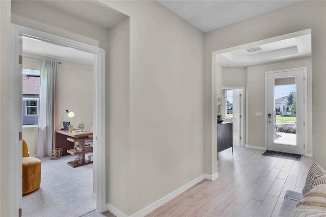 foyer with baseboards, visible vents, a raised ceiling, and light wood-style flooring