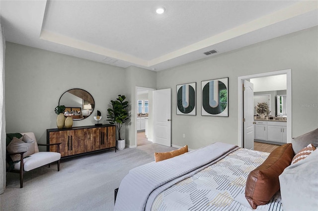 bedroom featuring light carpet, visible vents, baseboards, ensuite bathroom, and a tray ceiling