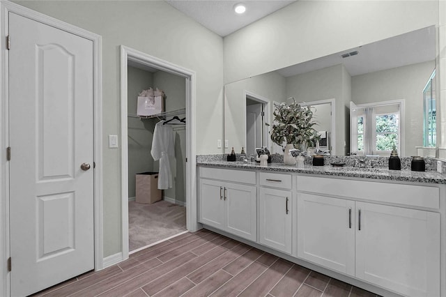 bathroom featuring a sink, visible vents, wood tiled floor, double vanity, and a walk in closet