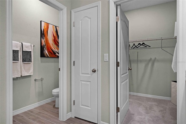 bathroom with wood finish floors, a walk in closet, toilet, and baseboards