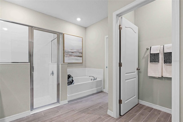 bathroom featuring wood tiled floor, baseboards, a bath, and a shower stall