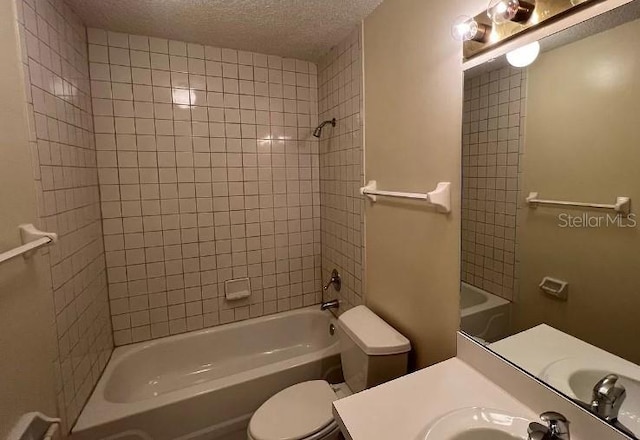 full bathroom with vanity, tiled shower / bath combo, toilet, and a textured ceiling