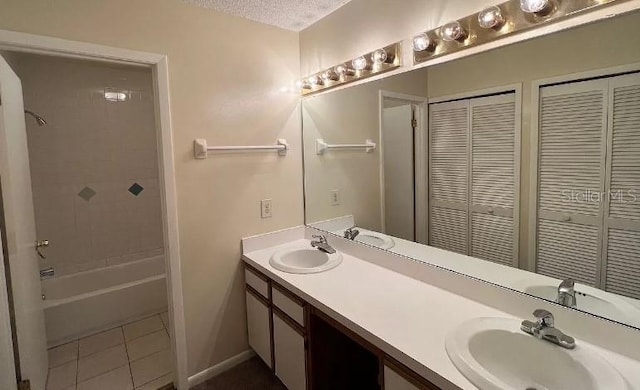 bathroom featuring tiled shower / bath, a textured ceiling, dual bowl vanity, and tile patterned flooring