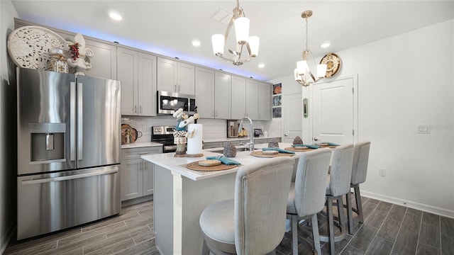 kitchen featuring decorative light fixtures, tasteful backsplash, dark hardwood / wood-style floors, appliances with stainless steel finishes, and a kitchen island with sink